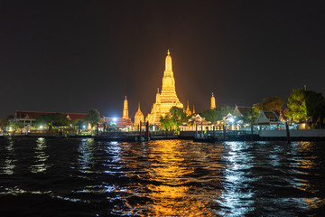 Naklejka premium Large illuminated temple Wat Arun after sunset seen accross river Chao Phraya Bangkok, Thailand.golden Buddha in side temple Wat Arun the biggest and tallest pagoda in the world