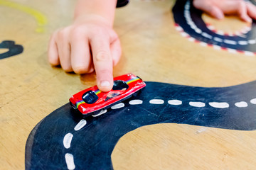 Child plays with two miniature cars in a toy circuit.