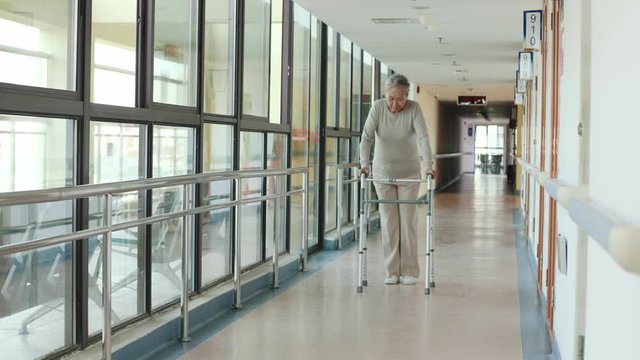 asian old woman walking using a walker in hallway of nursing home
