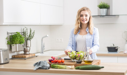 Obraz na płótnie Canvas Young happy blonde girl preparing healthy salad in home kitchen