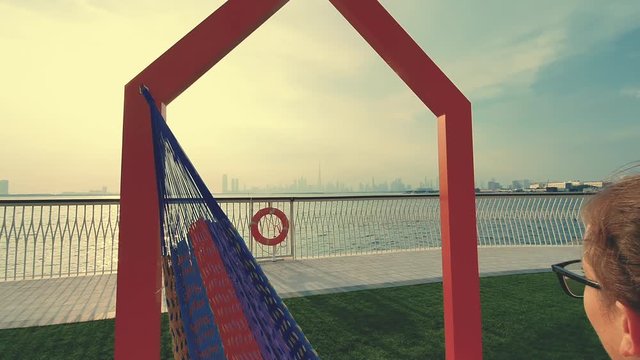Young woman weared in office sute having coffee in hammock while chilling , freelance life style conceptual, work anywhere. Modern city on the background.
