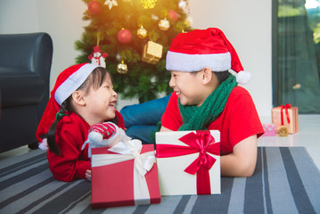 Fototapeta na wymiar Little asian girl and her brother lying on the floor with gift box and smiling together at home in Christmas holiday.