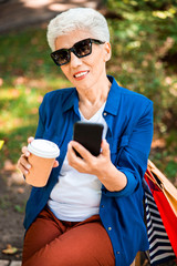 Smiling senior woman holding cellphone and cup of coffee