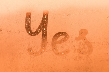 The creative inscription yes on the orange or pink evening or morning window glass with drops 