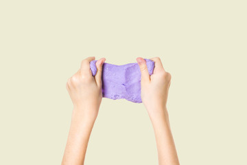 Lilac slime in the hands of a child on a light yellow background.