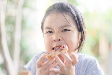 Funny little asian girl eating tasty toasts with strawberry jam spread for breakfast. Hungry face and Delicious face in kid girl.