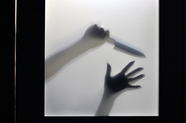 The concept of domestic violence in the family. Hand with a knife, shadows through the door glass.