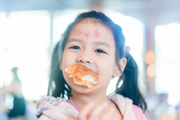 Cute little asian girl holding and eating soft bread at home.Hungry kid girl make delicious face when she eating bakery.