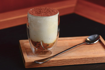 Traditional Italian dessert tiramisu in a glass served on a wooden board with a spoon in a restaurant. Italian cuisine