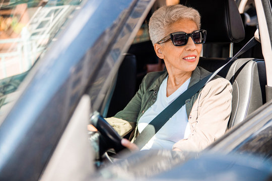 Joyful senior lady in sunglasses sitting in car