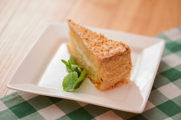 Slice of victoria sponge cake with cream filling, served with a mint leaf on a white plate on light wooden table