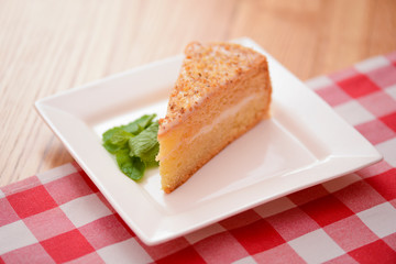 Slice of victoria sponge cake with cream filling, served with a mint leaf on a white plate on light wooden table