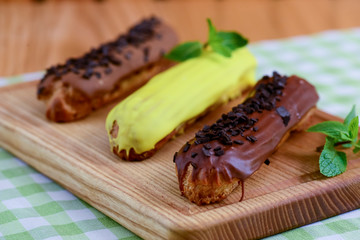 Traditional french dessert eclair pastry, three pieces laying on wooden board on a table covered with plaid fabric.