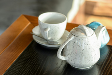 Tea cup with black tea on a small little plate with white tea pot on dark wooden table