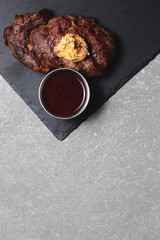 Grilled beef steak medium rare with sauce on black wooden cutting board. Top view, copy space, flat lay.