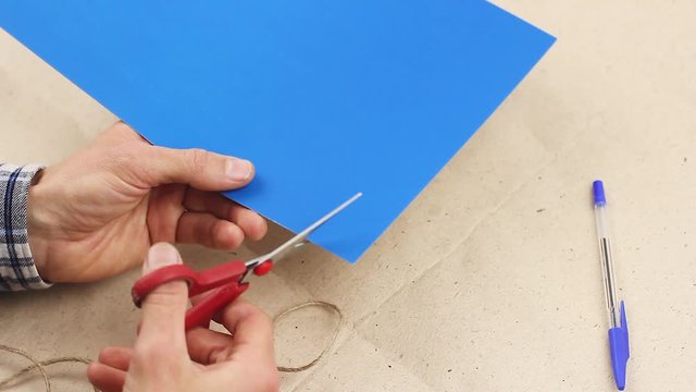 man tries to cut something out of blue paper with red scissors, make some craft work, but does not dare to do it, concept of indecision and hesitation or doubts, torment of creativity 