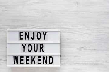 'Enjoy your weekend' words on a modern board on a white wooden surface, top view. Overhead, from above, flat lay. Space for text.