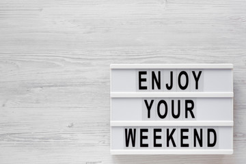 'Enjoy your weekend' words on a modern board on a white wooden background, top view. Overhead, from above, flat lay. Space for text.