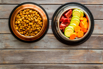 Healthy feed for cats and dogs. Bowls full of dry feed, meat and vegetables on dark wooden background top-down copy space