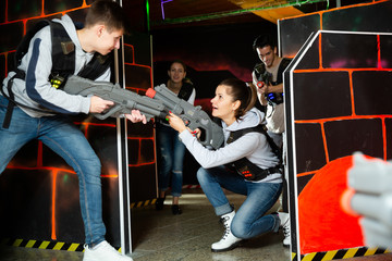 Excited young people playing enthusiastically laser tag game two teams opposite each other in dark room