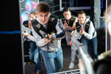 Portrait of happy young man with laser pistol and playing laser tag with his friends in dark room