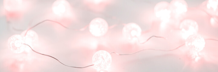 Obraz premium Pink christmas lights on white background for design. Festive decorations, white sparkling and glowing lights garland. Traditional winter holiday celebration accessories. Xmas backdrop with copyspace