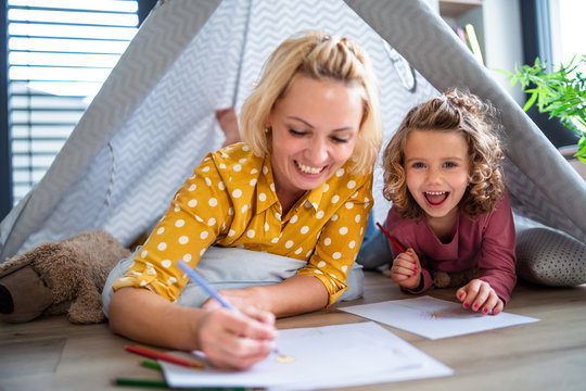 A cute small girl with mother indoors at home, drawing pictures.
