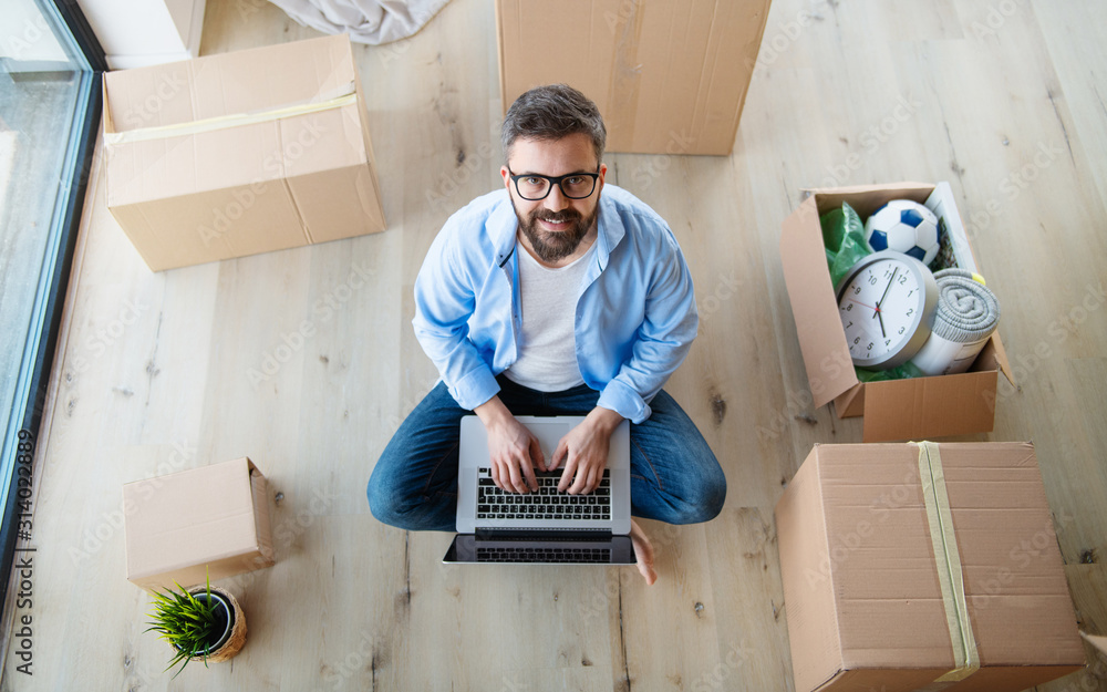 Wall mural Top view of mature man with boxes moving in new house, using laptop.