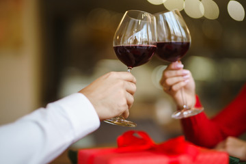 Hands holding glasses of wine on restaurant background. Couple clink glasses with red wine. Romance at restaurant for Valentine's Day- concept. Relationship & Birthday concept.