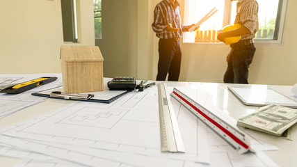 The house layout on the table with documents and background, with 2 engineers standing to talk.