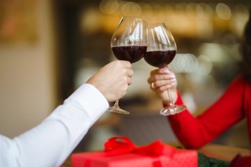 Hands holding glasses of wine on restaurant background. Couple clink glasses with red wine. Romance at restaurant for Valentine's Day- concept. Relationship & Birthday concept.