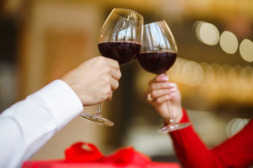 Hands holding glasses of wine on restaurant background. Couple clink glasses with red wine. Romance at restaurant for Valentine's Day- concept. Relationship & Birthday concept.