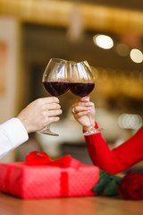 Hands holding glasses of wine on restaurant background. Couple clink glasses with red wine. Romance at restaurant for Valentine's Day- concept. Relationship & Birthday concept.