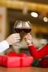 Hands holding glasses of wine on restaurant background. Couple clink glasses with red wine. Romance at restaurant for Valentine's Day- concept. Relationship & Birthday concept.