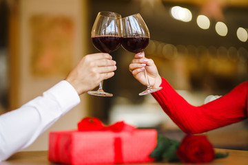 Hands holding glasses of wine on restaurant background. Couple clink glasses with red wine. Romance at restaurant for Valentine's Day- concept. Relationship & Birthday concept.