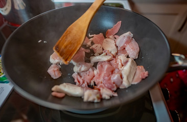  An unidentifiable home cook pan frying chicken in a black non-stick pan on the hob