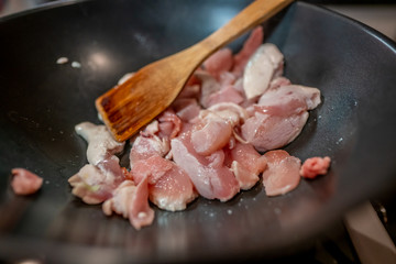  Close up of diced chicken pieces being pan fried in a black non-stick pan on the hob with a wooden...