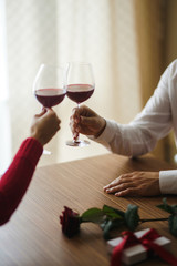 Hands holding glasses of wine on restaurant background. Couple clink glasses with red wine. Romance at restaurant for Valentine's Day- concept. Relationship & Birthday concept.