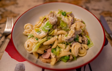 Selective focus of a leek, chicken and bacon pasta dish on a placemat on a dining table with a soft focus knife and fork