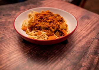 Close up of bowl of lentil spaghetti bolognese on a plain wooden background
