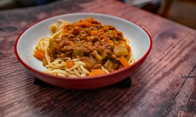  Close up of bowl of lentil spaghetti bolognese on a plain wooden background