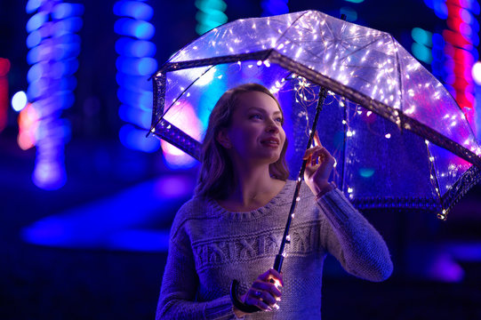 A girl walks through the night city with lights. Rainy. With an umbrella with lights.