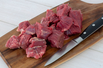 Beef brisket, diced cubed, on a wooden chopping board with a knife.  Grey wood background