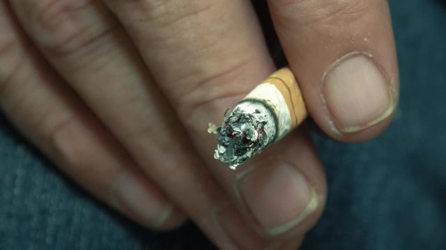 eine qualmende Zigarette wird in der Hand gehalten