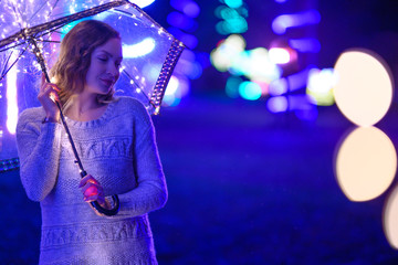 Woman or girl with umbrella with lights during the rain, lights and garlands. Rain atmosphere, art photo. Horizontal photo. With space