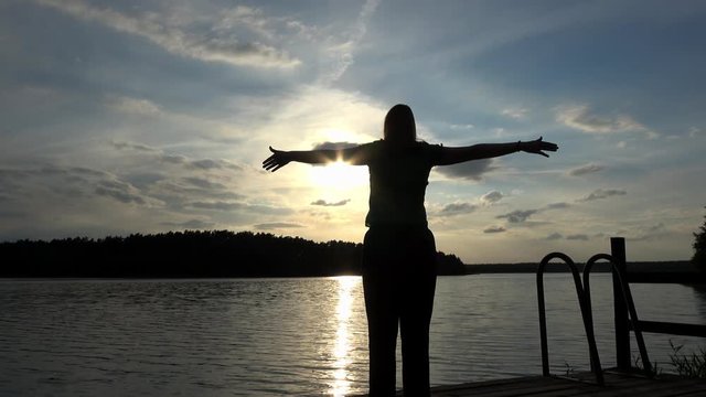 eine Frau steht bei Sonnenuntergang am See und macht Yoga