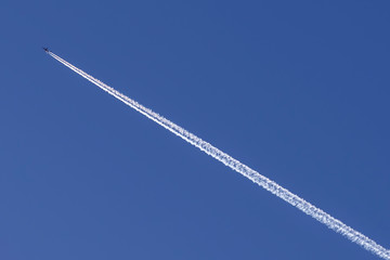 A plane crosses the blue sky diagonally leaving behind a long white trail