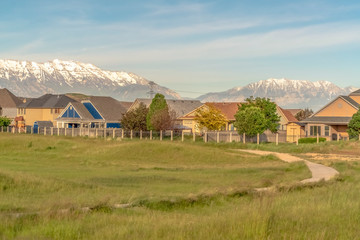 Narrow road and grassy terrain against homes and snowy mountain on a sunny day