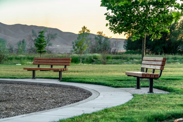 Benches and pathways at a park with lush green grasses and trees at sunset