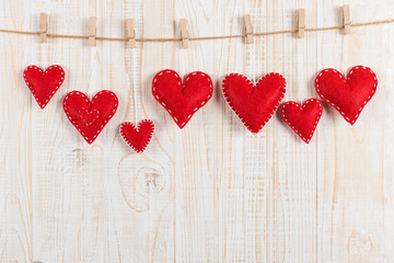 The concept of the preparation for Valentine's Day. Red hearts are held by clothespins on jute rope, on a white wooden background. Copy space.